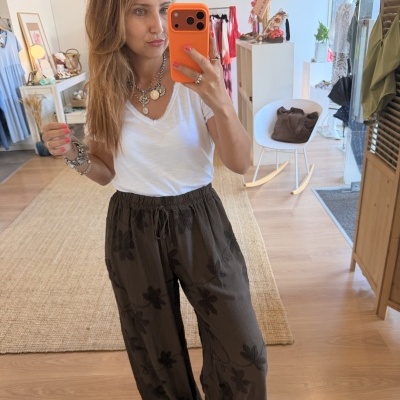 Mulher com t-shirt branca e calças castanhas com padrão floral num ambiente de loja de roupas.