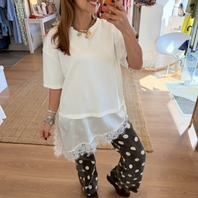 Pessoa a tirar selfie com telemóvel, vestindo t-shirt branca, calças cinzentas com bolas brancas e sapatos castanhos