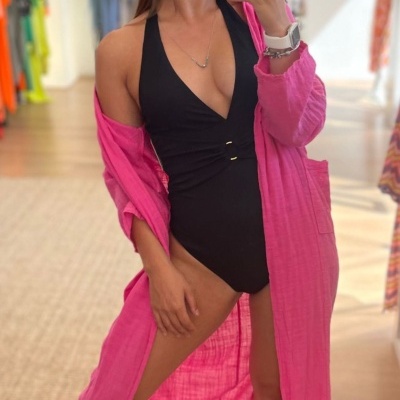 Mulher com fato de banho preto e saída de praia rosa a tirar selfie numa loja