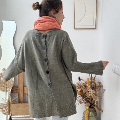 Mulher de costas com camisola cinzenta com botões, cachecol salmão, jeans e botas pretas em ambiente interior decorado.