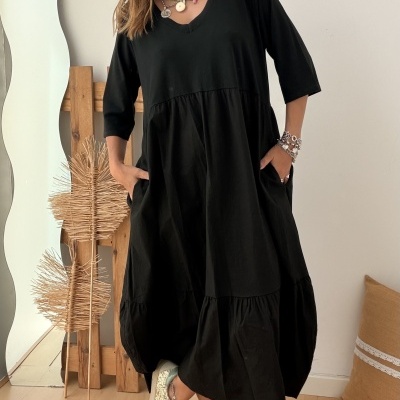 Mulher com vestido preto solto de manga 3/4 e sapatilhas brilhantes em chão de madeira clara
