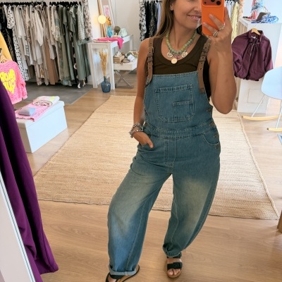 Mulher a tirar selfie com macacão em ganga azul claro e alças castanhas num espelho de loja de roupa.