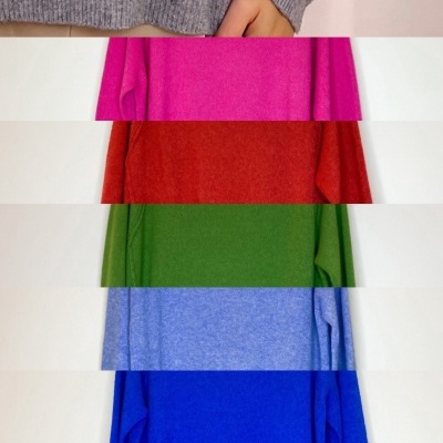 Várias camisolas de manga comprida em diferentes cores lisas penduradas numa parede.