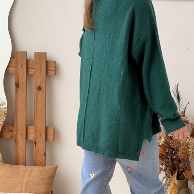 Mulher de costas com camisola verde e calças de ganga bordadas em ambiente interior