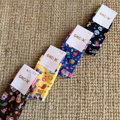 Pares de meias coloridas com estampas de caveiras e flores e etiquetas GNC-X sobre tapete de fibra natural