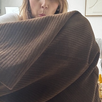 Manta castanha canelada exibida por mulher com camisa branca