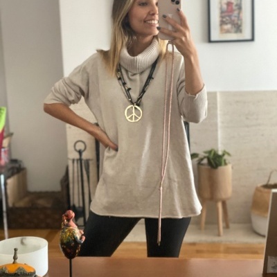 Mulher com camisola bege de gola alta a tirar selfie numa divisão com decoração