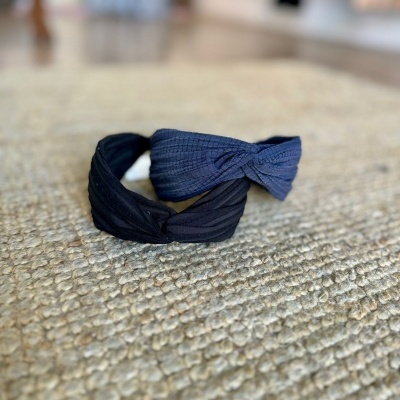 Duas tiaras de tecido preto e azul escuro com nó torcido sobre tapete bege