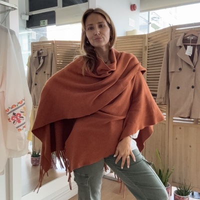 Mulher com capa laranja e calças verdes numa loja com cortinas e cabides