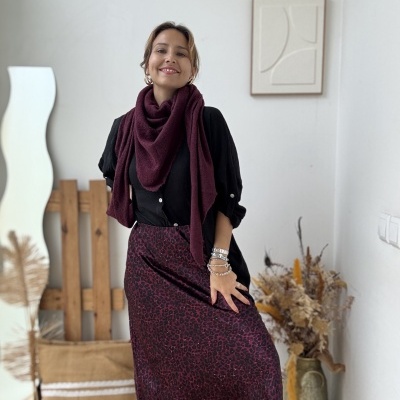 Mulher com blusa preta e saia estampada vinho e preto com cachecol vinho em ambiente rústico