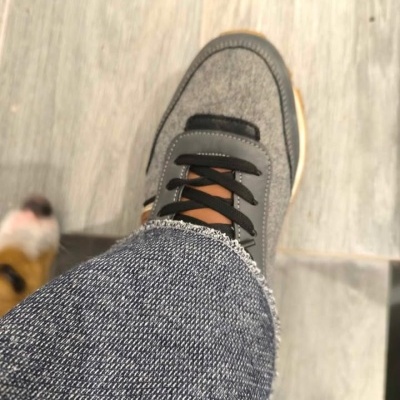 Sapatilha cinzenta com atacadores pretos e sola clara sobre chão cinzento e jeans azul