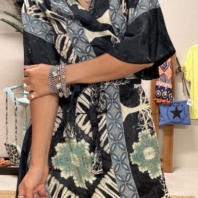 Vestido feminino leve com padrão floral em tons de preto e verde, acessórios prateados e brincos grandes, cenário interno com prateleira colorida