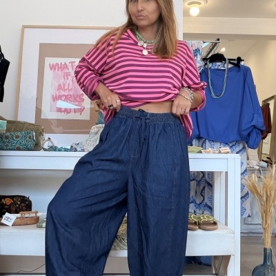 Mulher com camisola rosa às riscas, calças largas azul-escuro e sapatilhas brancas numa loja de roupa.