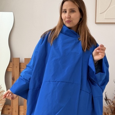 Mulher com capa azul oversized em ambiente interior com parede branca