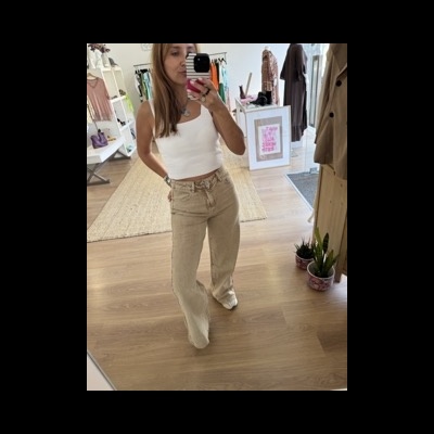 Mulher com top branco e calças largas creme a tirar selfie num espelho numa loja clara e organizada