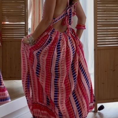 Vestido comprido colorido com alças e costas abertas, refletido num espelho, usado por mulher em ambiente interior