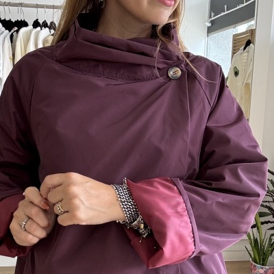 Casaco impermeável roxo com gola alta e botão prateado, manga virada com forro vermelho.