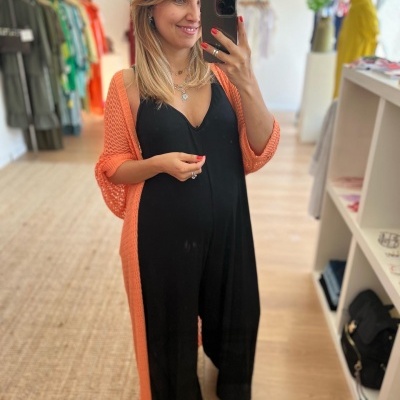 Mulher vestindo macacão preto e cardigan laranja num ambiente de loja de roupa