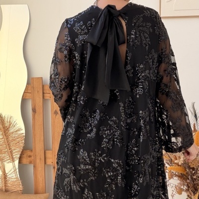 Vestido preto bordado com laço nas costas em ambiente interior