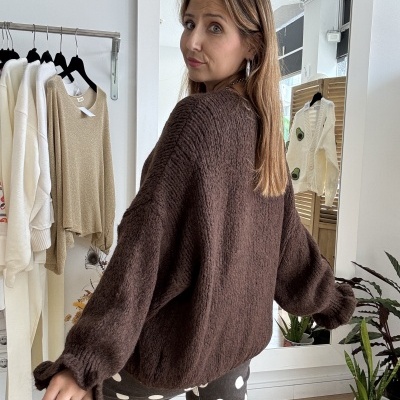 Casaco castanho de malha grossa com manga larga e calças cinzentas de bolas brancas em ambiente interior