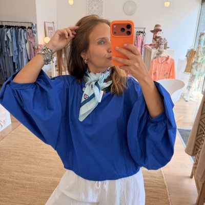 Mulher a tirar selfie com blusa azul e lenço azul claro na loja de roupa