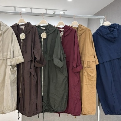 Cinco casacos compridos com capuz em várias cores pendurados numa estrutura metálica