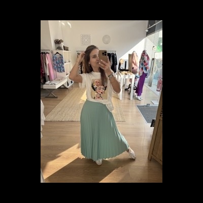 Mulher com t-shirt estampada e saia plissada numa loja de roupa.