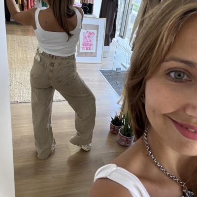 Mulher em roupa casual tirando selfie num espelho com calças largas bege e top branco