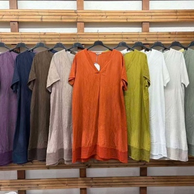 Doze vestidos de manga curta em várias cores pendurados em cabides pretos contra uma parede com ripas de madeira