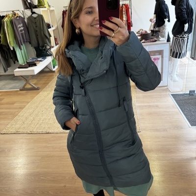 Mulher com casaco azul acolchoado a tirar selfie numa loja de roupa.