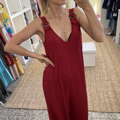 Mulher a usar macacão vermelho com alças e fivelas, foto em ambiente com roupas ao fundo