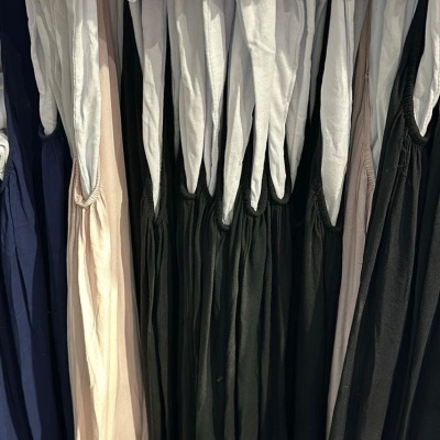 Várias peças de roupa penduradas com alças brancas em diferentes cores e tecidos leves