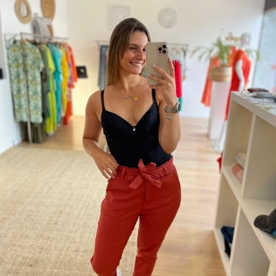 Mulher em loja de roupa tirando selfie com telemóvel, top preto e calças vermelhas com laço