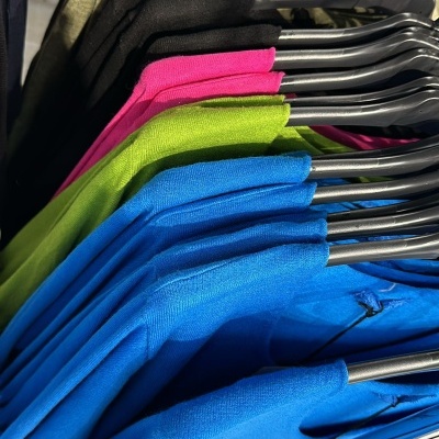 Camisetas coloridas penduradas em cabides pretos numa estrutura metálica