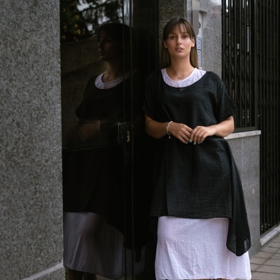Mulher com vestido branco e sobreposição preta encostada em porta de vidro