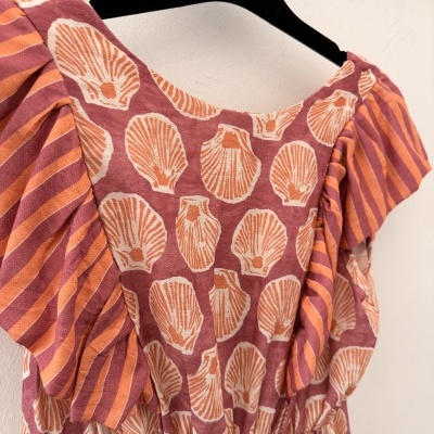 Vestido de mulher com padrão de conchas e mangas às riscas, pendurado em cabide preto