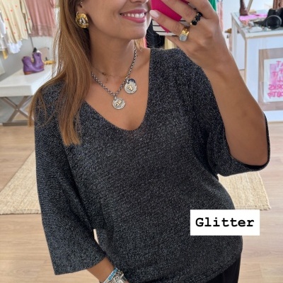 Mulher a tirar selfie vestindo camisola preta com glitter e calças pretas numa loja de roupa