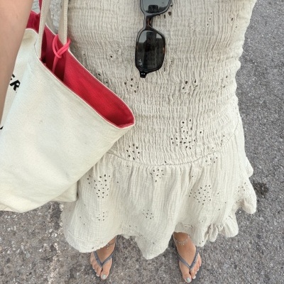 Vista de cima para baixo de vestido branco creme texturizado com óculos de sol presos e bolsa de tecido branca com interior vermelho, sandálias pretas.
