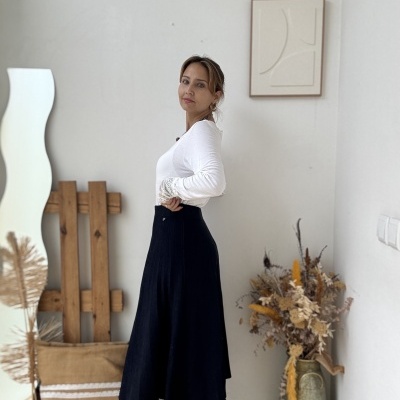 Mulher com blusa branca, saia preta e botas pretas em ambiente com decoração minimalista