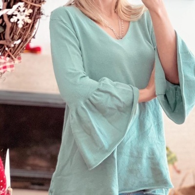 Mulher a tirar selfie com blusa verde água e calças de ganga em ambiente interior com decoração natalícia