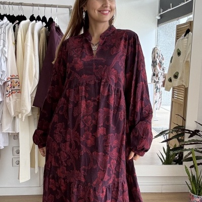 Vestido bordô de padrão floral com mangas compridas num ambiente interior com cabides e plantas