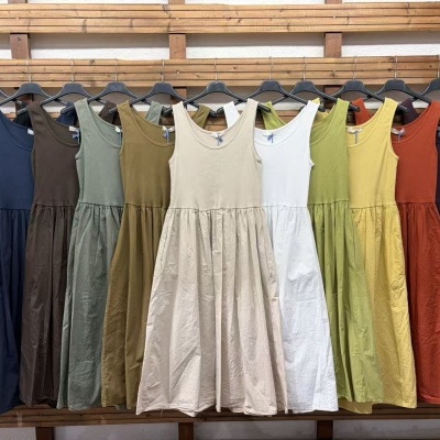 Vestidos coloridos sem mangas pendurados em cabides pretos na parede de madeira.