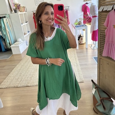 Mulher num vestido branco com sobreposição verde numa loja de roupa com vestidos coloridos ao fundo