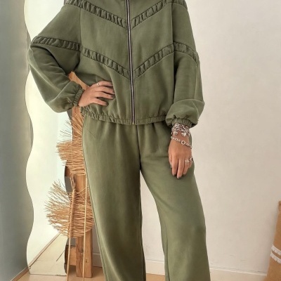 Conjunto verde musgo com casaco e calças largas, mulher com pulseiras prateadas e ténis brancos com detalhes brilhantes.