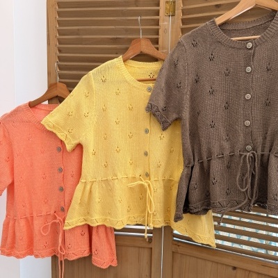 Três cardigans de malha coloridos pendurados em cabides de madeira