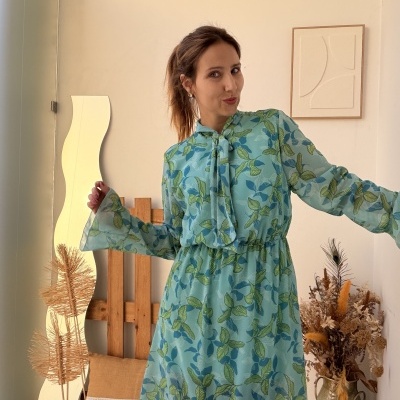 Vestido azul claro com folhas verdes e azuis, tecido leve transparente e gola com laço