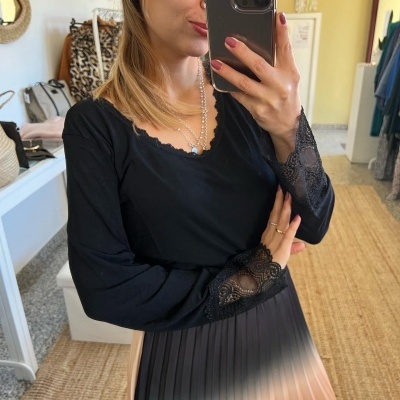 Mulher com blusa preta com renda e saia plissada em degradê bege e castanho