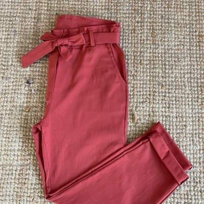 Calças rosa dobradas com cinto e laço sobre tapete bege texturizado