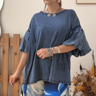 Mulher com blusa azul e calças estampadas em interior com flores secas