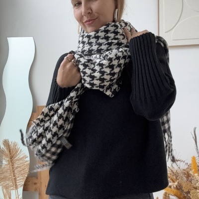 Mulher de camisola preta e cachecol xadrez preto e branco em ambiente interior com decoração seca.